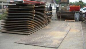 Mehrere Stahlplatten zum Kauf sind aufgestapelt zu sehen und eine Stahlplatte zum Kauf liegt auf dem Boden.